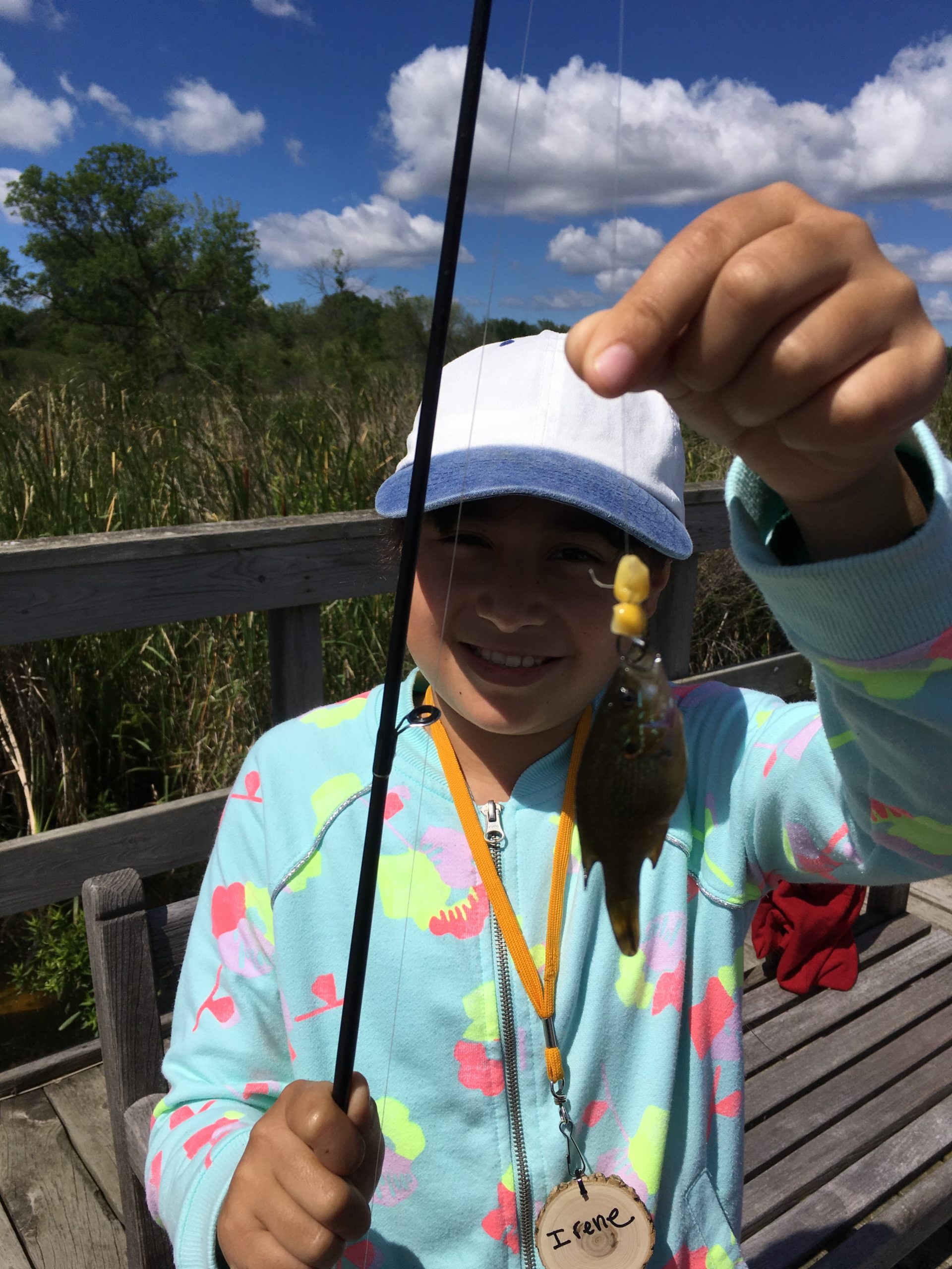 girl with fishing pole holding up fish she caught