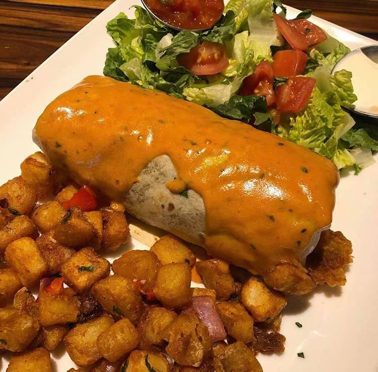 breakfast burrito covered in cheese sauce with breakfast potatoes