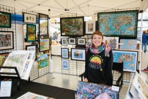 woman displaying her artwork in a booth at the art fair