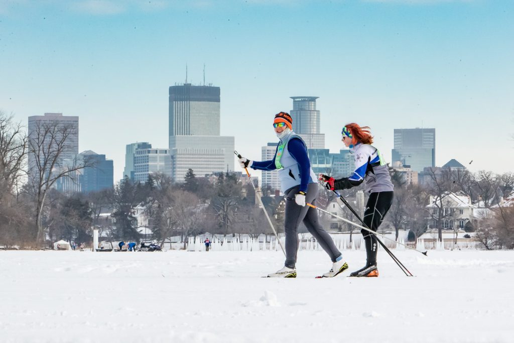 Two people racing in a loppet at Theo Wirth with downtown Minneapolis in the background