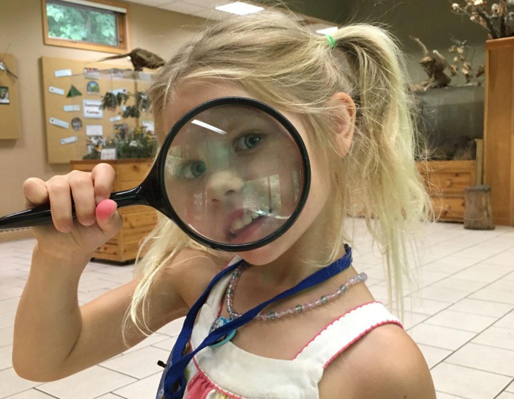 Girl looking through a magnifying glass at Westwood Hills Nature Center