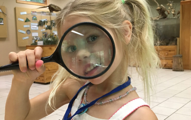girl looking through magnifying glass at the nature center