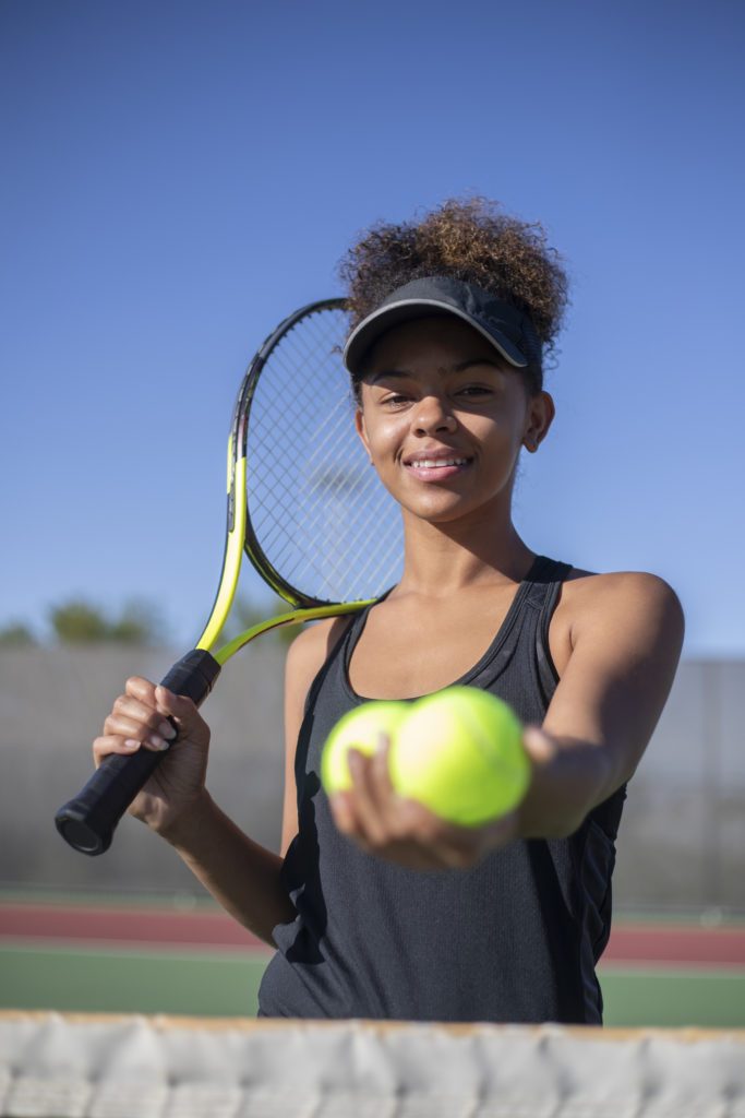 girl holding a tennis racquet and 3 tennis balls