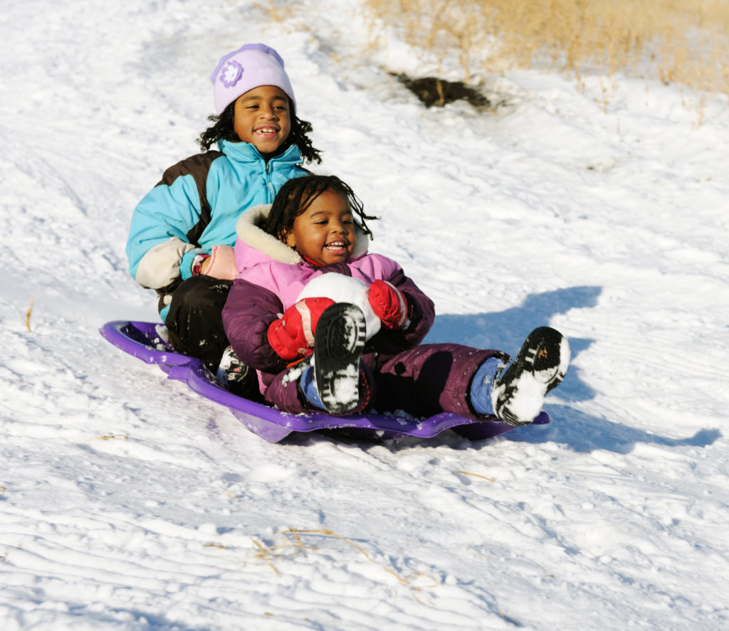 two girls on a sled going down a hill