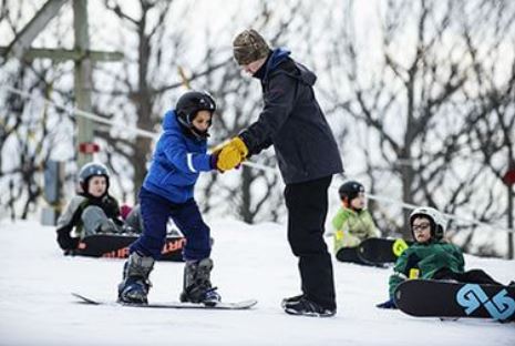 man teaching kids to snowboard