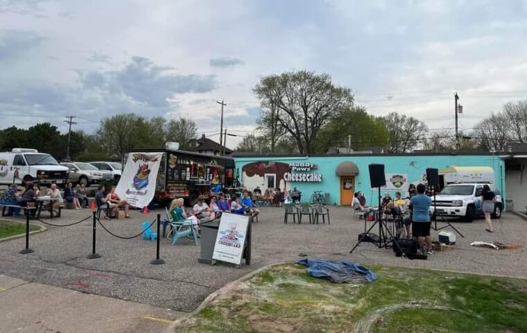 A view of the Muddy Paws parking lot with food trucks, a musician playing and people eating.